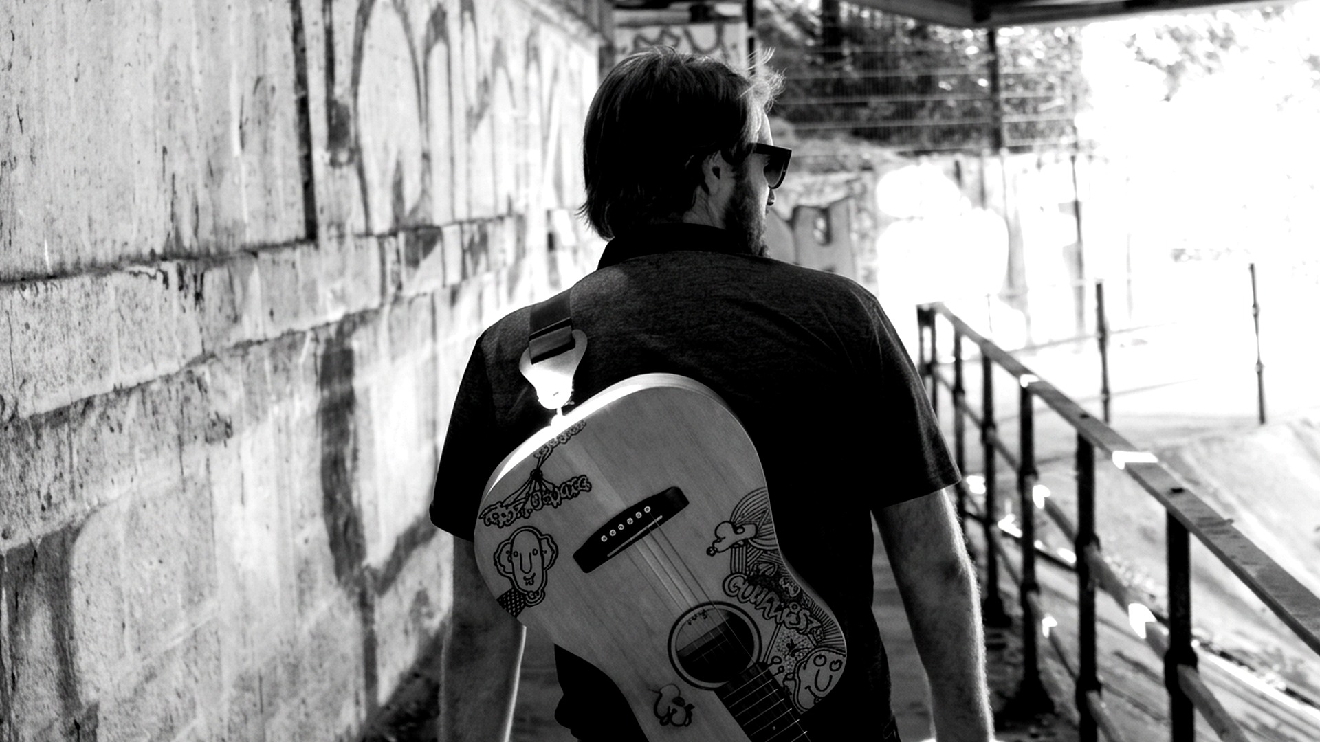 Marty de dos, guitare sur l'épaule, dans un passage sous un pont