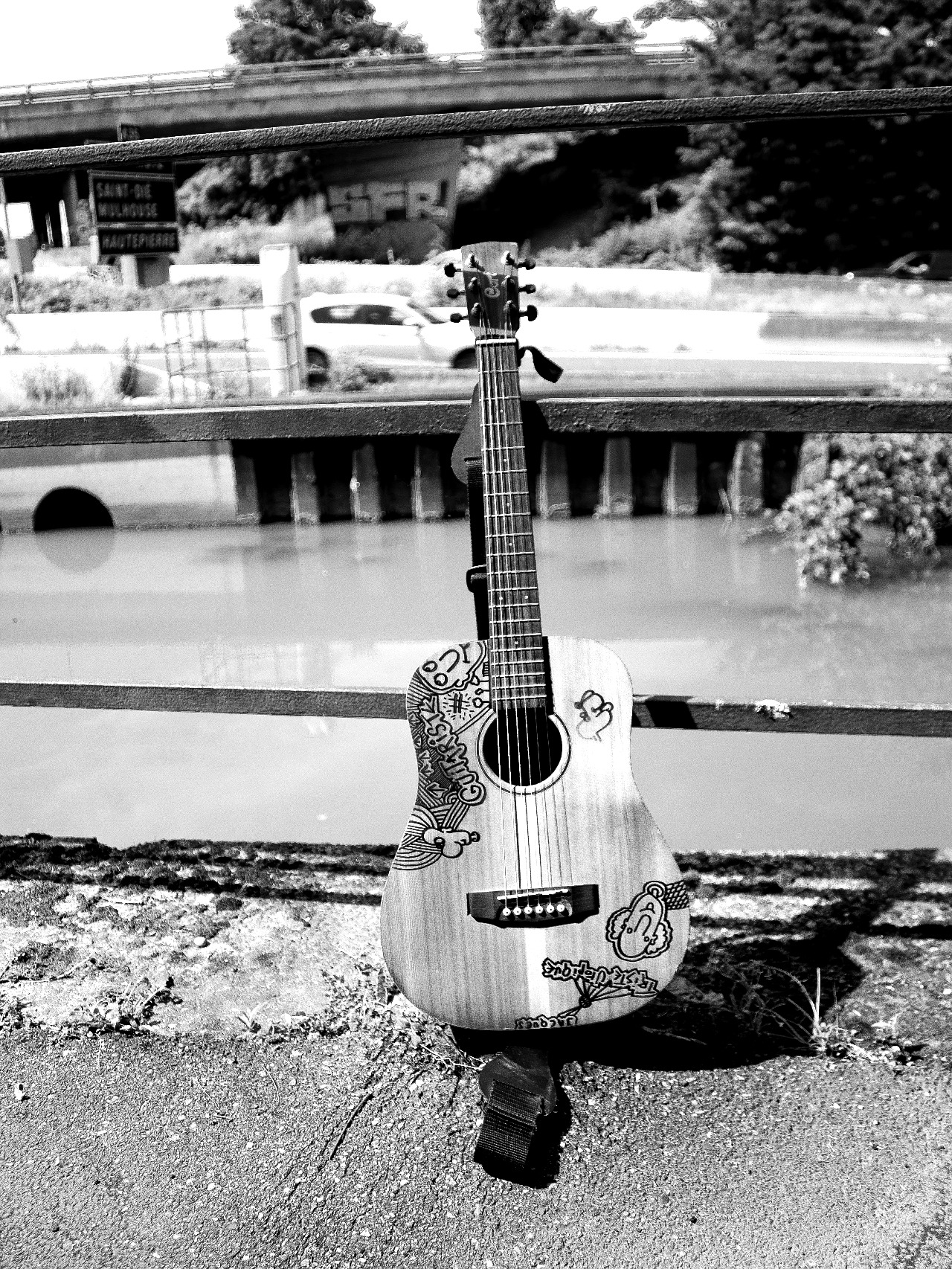 Guitare acoustique illustrée, posée contre une rambarde au bord de l'eau